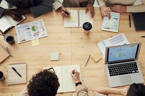 Équipe réunie autour d’une table de travail, dossiers et ordinateur portable.