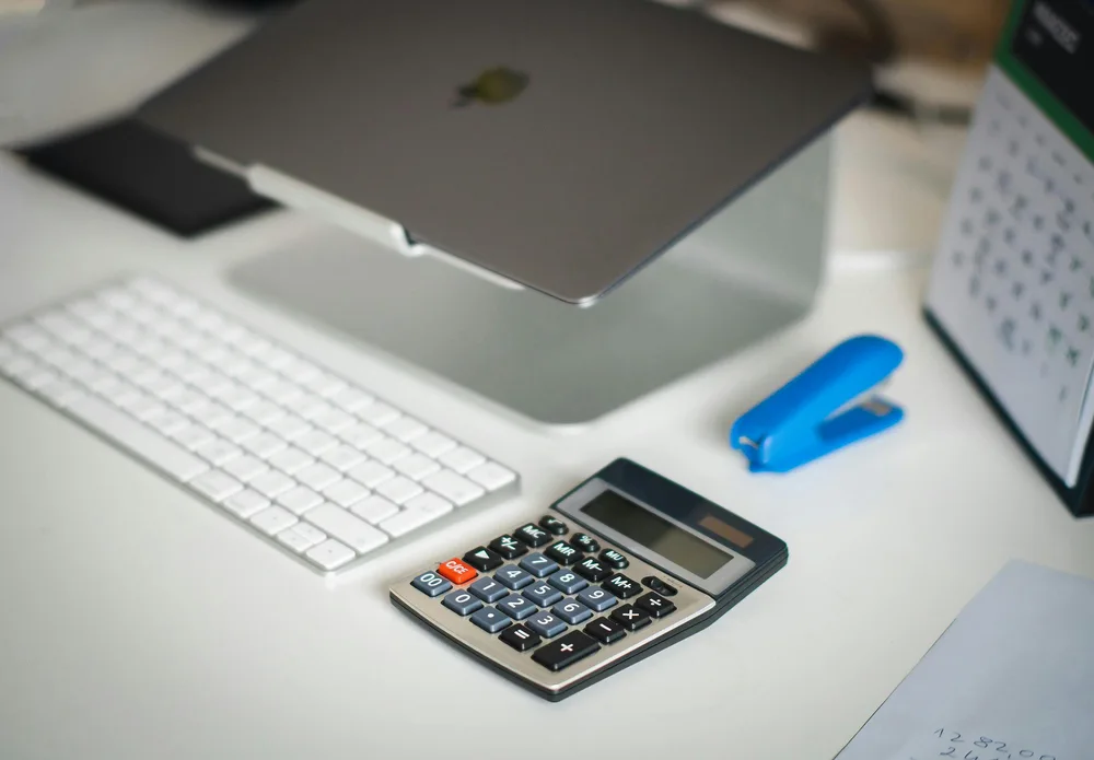 Ordinateur portable, clavier et calculatrice sur un bureau blanc.